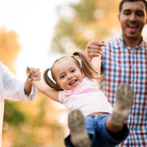 Parents swing their laughing daughter by the hands while walking outdoors in a park